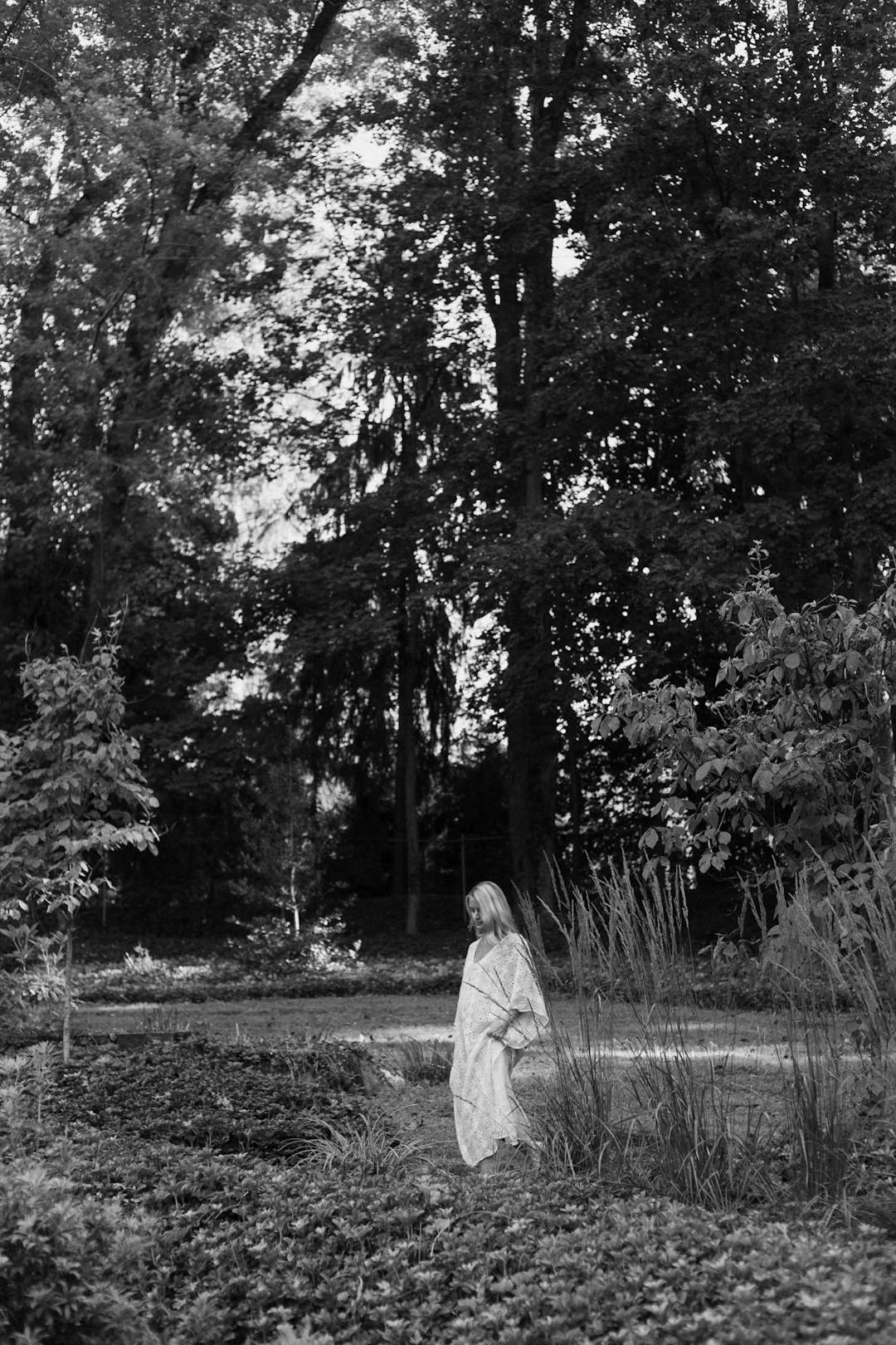 black and white medium format maternity portrait of woman in white dress walking in nature from a distance