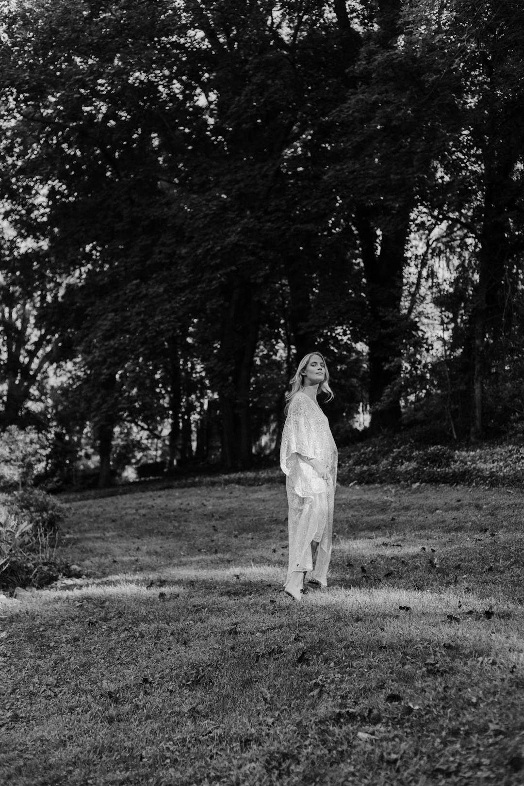 black and white medium format maternity portrait of woman in white dress walking in nature from a distance