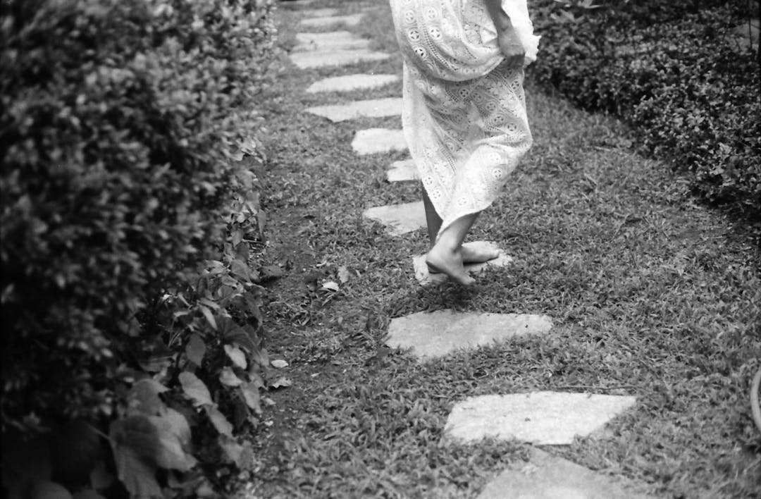 black and white film picture of woman in white dress walking along stones