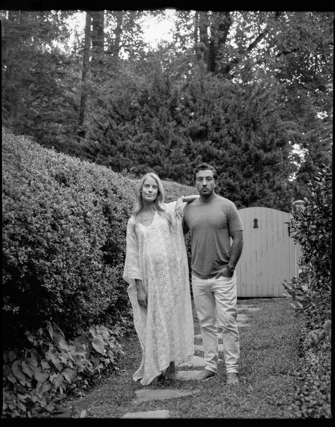 black and white medium format maternity portrait of woman in white dress holding belly with man 