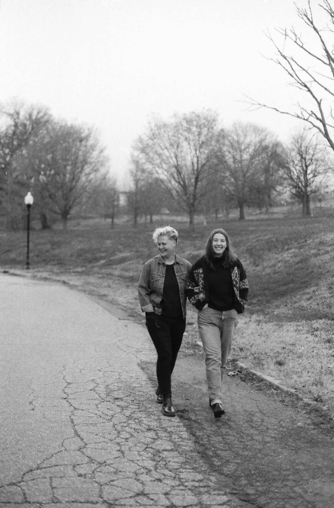 black and white film photo of two woman walking down path holding hands