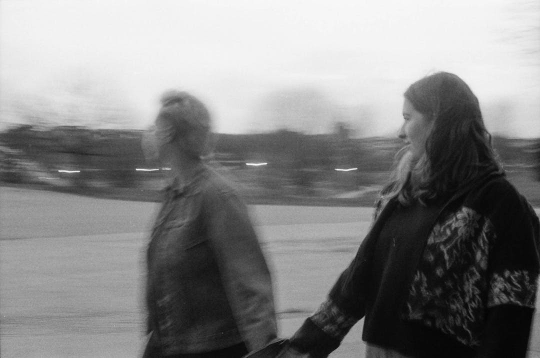 blurry black and white film photo of two woman holding hands while walking