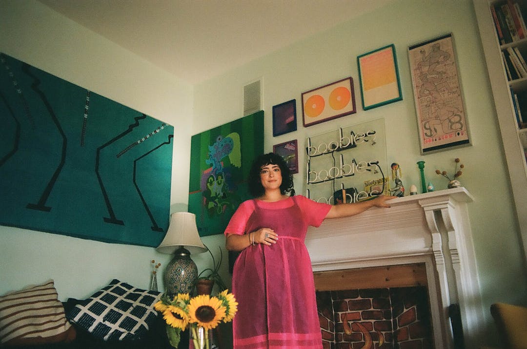 color film photo of woman in pink dress in colorful home leaning on mantle