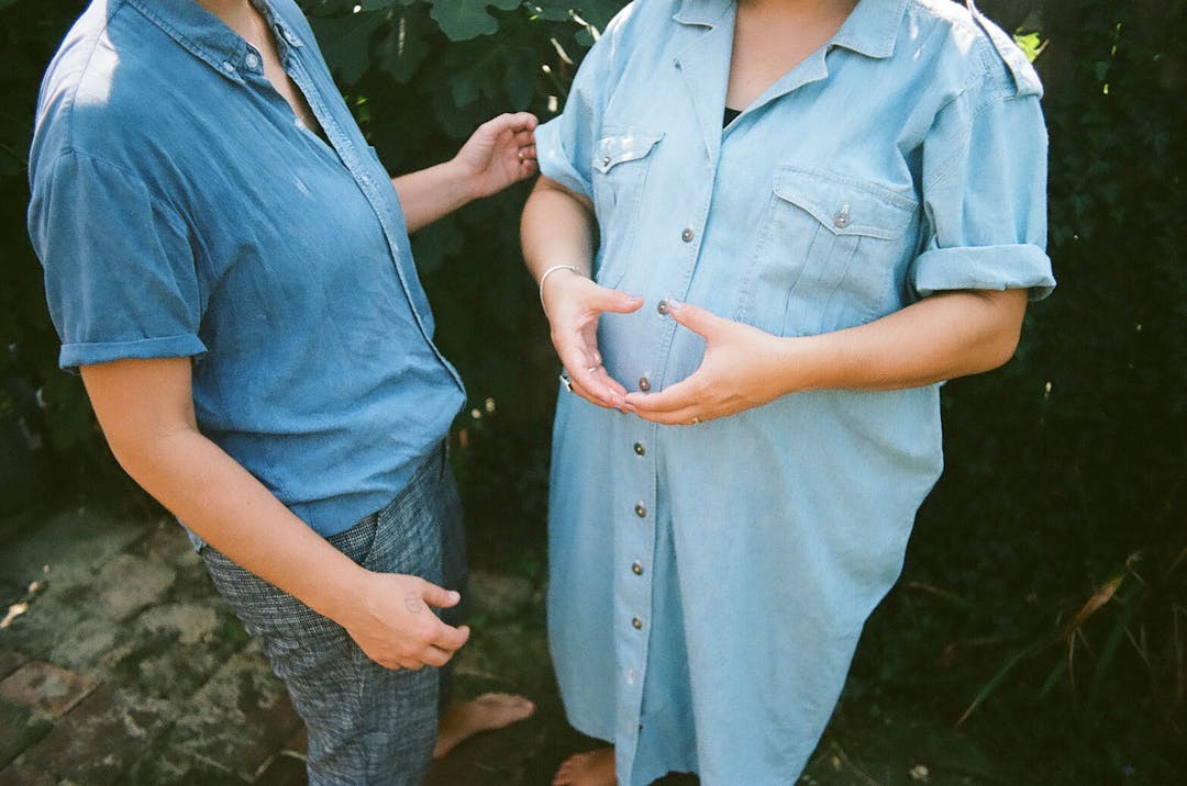"color photo of two woman in blue denim, one making the shape of a circle with her hands"